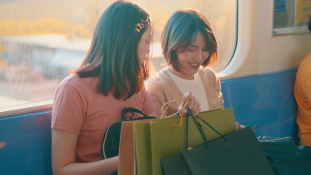 两个年轻的亚洲女人在火车上一边聊天一边用手机，慢镜头视频素材