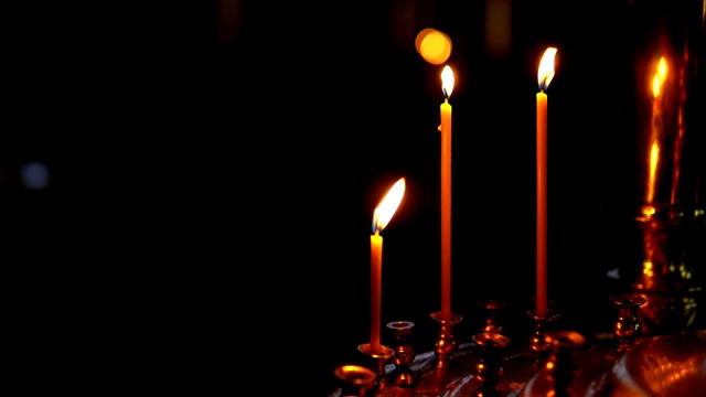 在黑暗背景下的教堂里，三支燃烧着的蜡烛插在一个金色的烛台上。视频素材