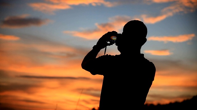 一个男人站在日落前拍照。视频素材
