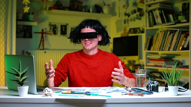 一个戴假发和黑眼镜的男人坐在办公室的一张桌子旁。视频下载