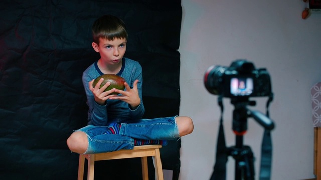 一个男孩坐在摄像机前，拿着一个芒果视频下载