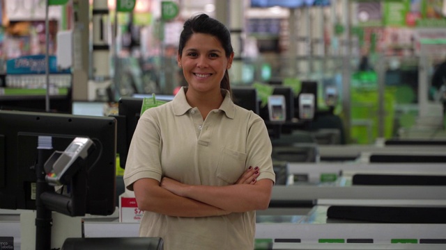 拉丁美洲的女收银员在超市，对着镜头微笑，同时交叉手臂视频下载