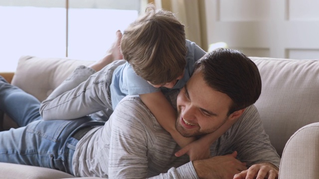 儿子抱着父亲背着孩子在沙发上看镜头视频素材