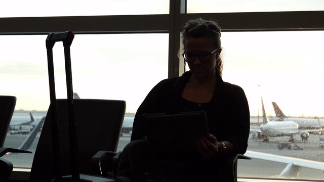 女人坐在机场休息室里用平板电脑，窗户后面有飞机视频素材
