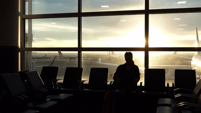 女人坐在机场休息室里用平板电脑，窗户后面有飞机视频素材