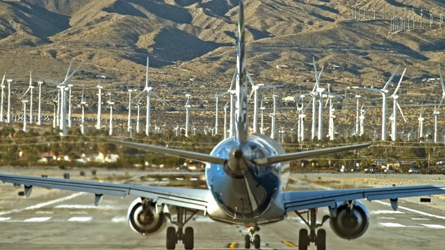 极长的镜头后视图阿拉斯加航空公司喷气式飞机制造转向机场跑道作为喷气式发动机排气充满空气的背景下，清洁能源风力农场在远处视频素材