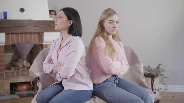 侧视图的成年白人深色头发的女人和十几岁的女孩背靠背坐在沙发上。母亲和女儿吵架了。家庭关系，冲突，问题。视频素材