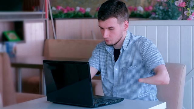 疲惫的残疾人与截肢的两个残手在咖啡馆工作类型的笔记本电脑。视频下载