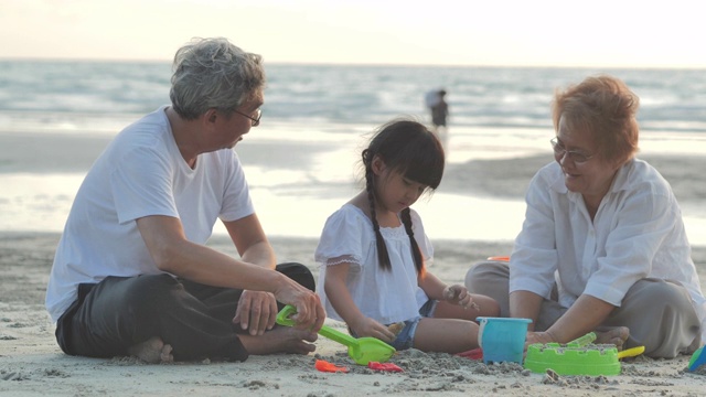快乐的爷爷、奶奶和孙女在沙滩上的沙箱里为孩子们玩玩具。家庭，生活方式，人，老人，人寿保险，假期，关系，假期，孩子，退休，健康保健理念。视频下载