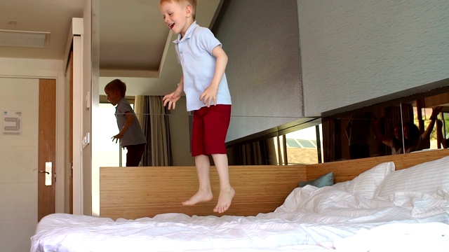 一个勇敢的小男孩在家里的床上又蹦又跳。缓慢的运动。视频下载