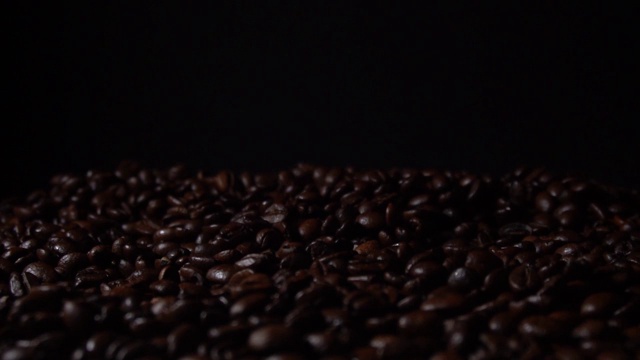 黑色背景下，新鲜烘焙的咖啡豆缓缓落下视频素材