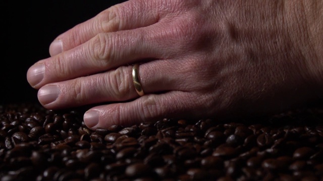 近距离的手采取新鲜烤咖啡豆让他们落在黑色背景的慢动作视频素材