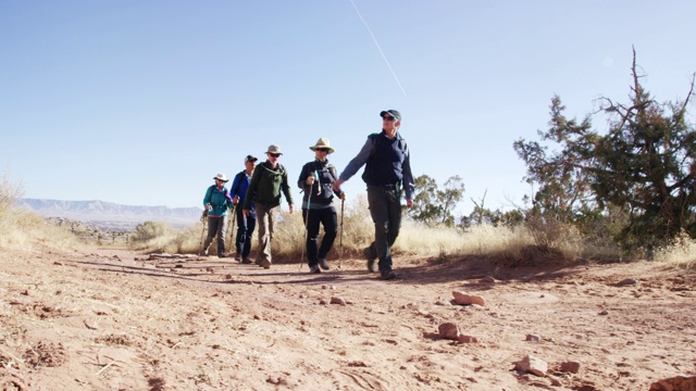 在一个晴朗、阳光明媚的日子里，一小群成熟的白人男性和女性一起在科罗拉多州西部的落基高沙漠山脉徒步旅行，背景是科罗拉多国家纪念碑视频下载