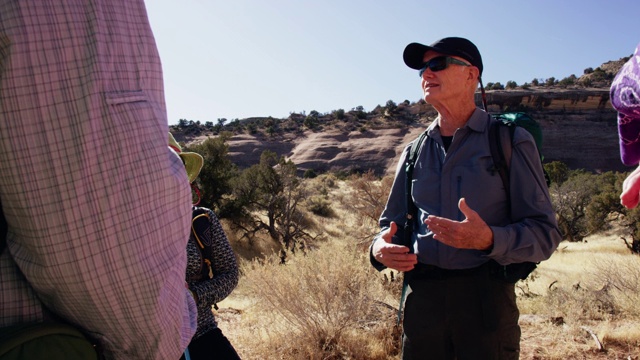 一个成熟的白人男子在他的七十多岁的谈话和大笑与一小群白人男人和女人，而一起在科罗拉多州西部的岩石高沙漠山在一个晴朗，阳光明媚的日子视频下载