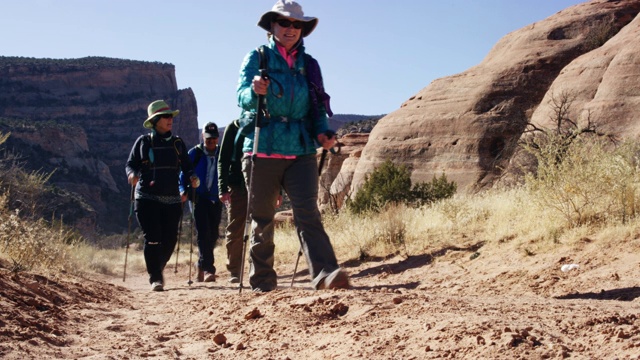 在一个晴朗、阳光明媚的日子里，一小群成熟的白人男性和女性一起在科罗拉多州西部的落基高沙漠山脉徒步旅行，背景是科罗拉多国家纪念碑视频下载