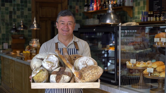 快乐成熟的面包店老板展示了一个篮子的面包，同时对着镜头微笑视频下载