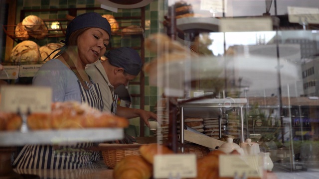 一家面包店的老板，一名男子在清洁柜台，一名女子在一边聊天一边微笑着安排面包陈列视频下载