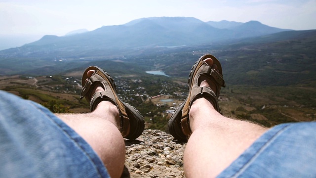 男人的腿在棕色的鞋子躺在岩石上的山的背景视频下载