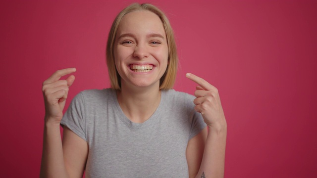 金发女孩是有趣的和膨出她的脸颊在粉红色的墙壁背景视频下载