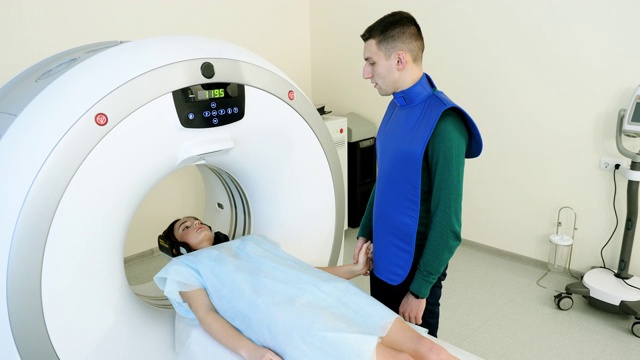 计算机断层扫描或磁共振成像的程序。女病人正在接受医学检查。CT或MRI扫描。帅哥牵着女友的手安慰她。4 k视频下载
