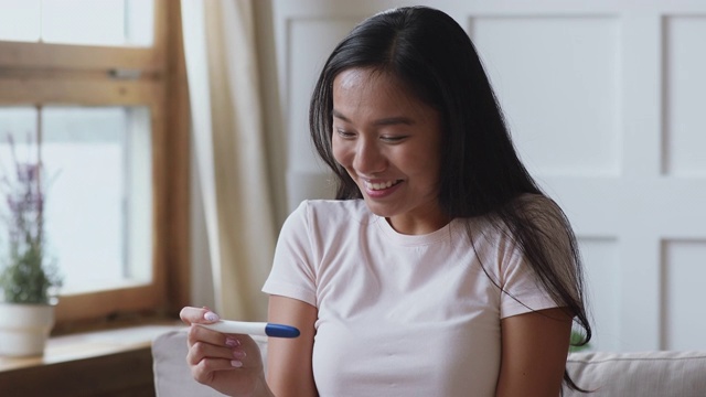 兴奋的年轻亚洲妇女拿着阳性怀孕测试在家视频素材