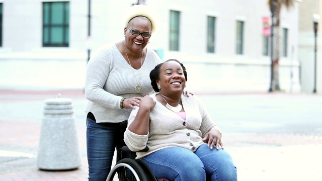 坐在轮椅上的女人和年迈的母亲在城市街道上视频下载