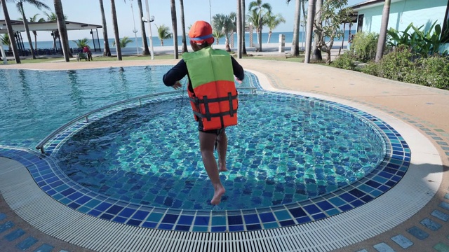 快乐的亚洲孩子男孩穿救生衣和泳衣戴泳镜跳进游泳池度假。节日快乐。慢动作视频下载