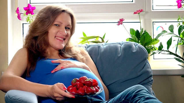 漂亮的孕妇吃着草莓，微笑着看着镜头视频素材