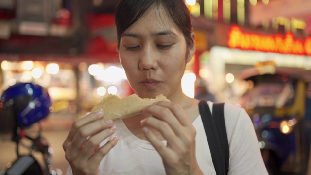 街头小吃-年轻女子在吃酥脆的煎饼在瑶华路，曼谷，泰国视频素材