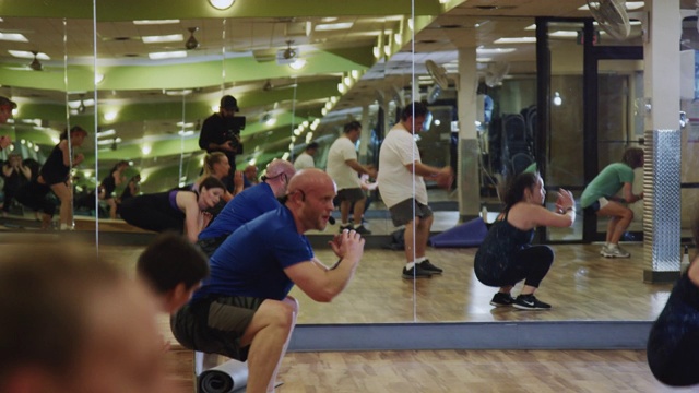 一位40多岁的白人健身教练在健身房里和他的团体健身班一起做下蹲跑步视频素材