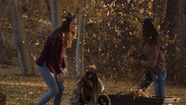 顽皮的女孩互相扔秋天的叶子的慢动作/雪松山，犹他州，美国视频素材