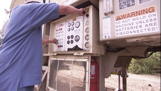 一名工人操作着仪表板，放下一对千斤顶来支撑一辆拖车，完成后关闭设备。视频下载