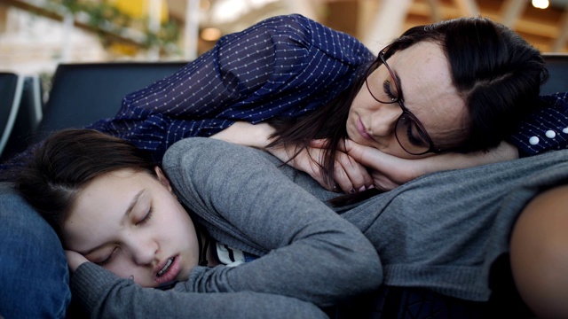 一个带着十几岁女儿的女人在机场候机室因疲惫而睡觉。航班的取消。视频素材