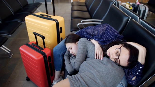 女人和十几岁的女儿一起睡在机场的椅子上等待出发。视频素材