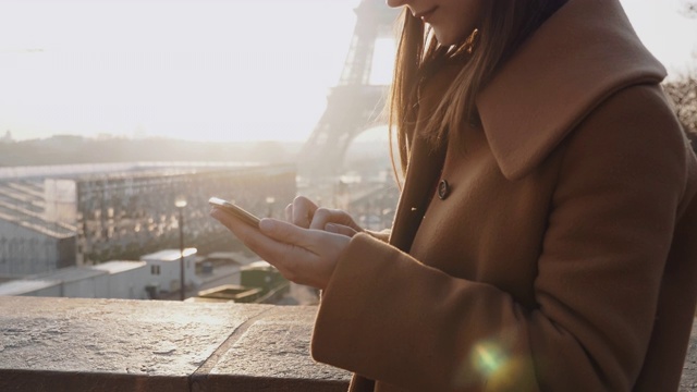 美丽的年轻专注的黑发女商人在阳光明媚的巴黎埃菲尔铁塔使用手机移动办公应用程序的慢动作。视频素材