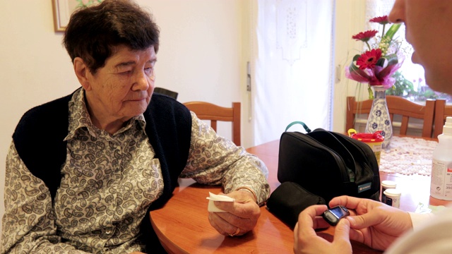 医护人员向微笑的老年妇女展示血糖检测结果视频下载