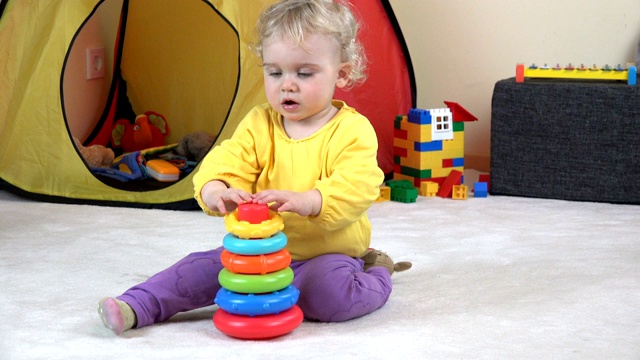 卷头发的小女孩玩着五颜六色的儿童金字塔。视频下载