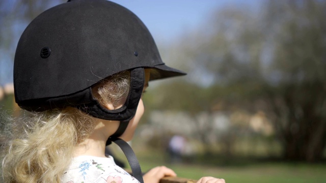 可爱的金发女孩戴着保护头盔等待骑马。万向节运动视频下载