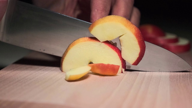 特写镜头切苹果。一个男人在厨房的砧板上切红苹果。视频下载