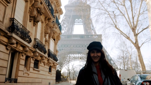 镜头跟随快乐美丽的女子兴奋地看到埃菲尔铁塔，在秋天的巴黎街头摆姿势微笑的慢镜头。视频素材
