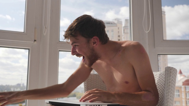 快乐快乐的白人男性玩家穿着内裤在笔记本电脑上玩在线视频游戏并获胜，举起双手欢呼视频素材