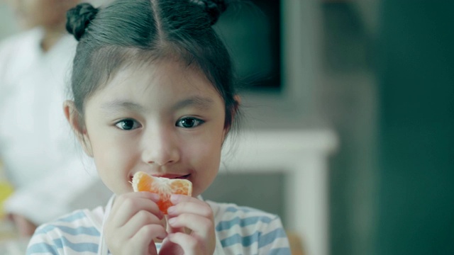 泰国可爱的小女孩拿着橘子，正面地看着镜头视频下载