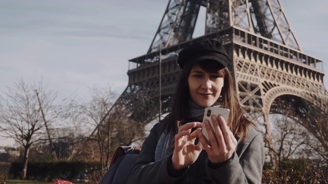 美丽微笑的年轻欧洲女子在阳光明媚的秋天巴黎埃菲尔铁塔附近使用智能手机购物应用程序的慢镜头。视频素材