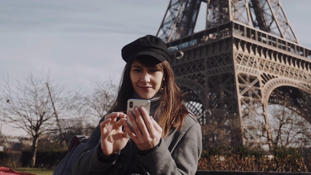 美丽年轻的欧洲女商人在阳光明媚的巴黎埃菲尔铁塔使用智能手机移动办公应用程序慢镜头。视频素材