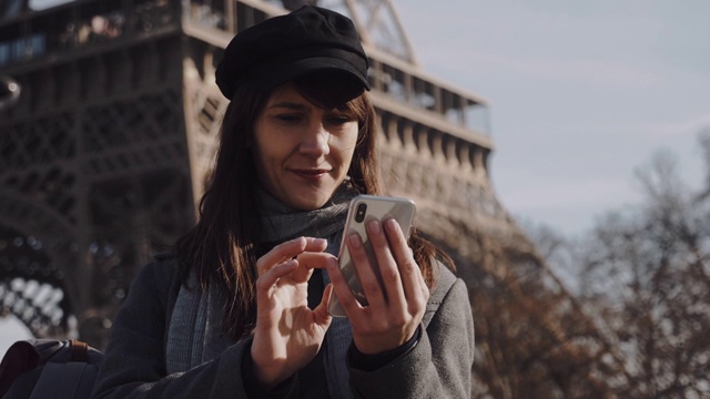 迷人的年轻欧洲女商人使用智能手机移动办公应用程序，思考着巴黎埃菲尔铁塔的慢镜头。视频素材