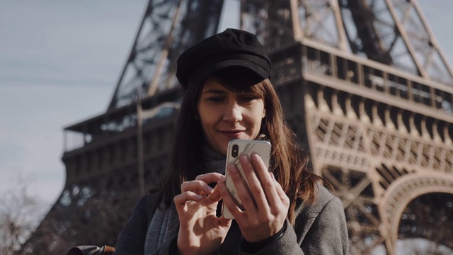 年轻的欧洲女游客微笑着使用智能手机社交网络应用程序拍摄著名的巴黎埃菲尔铁塔的慢镜头。视频素材