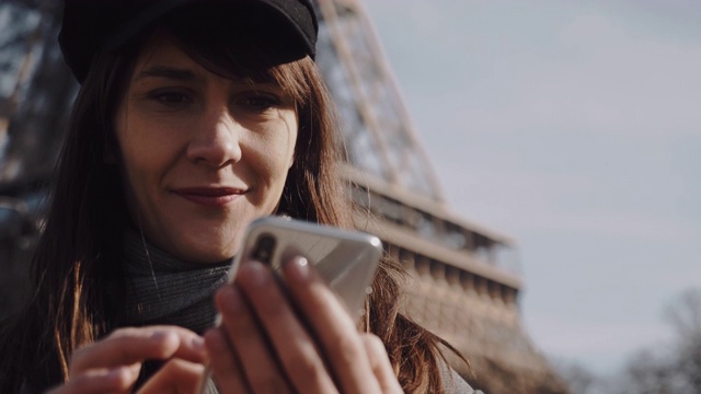 这是一幅美丽的年轻女商人使用智能手机购物应用程序，微笑着面对阳光明媚的巴黎埃菲尔铁塔的慢镜头视频素材