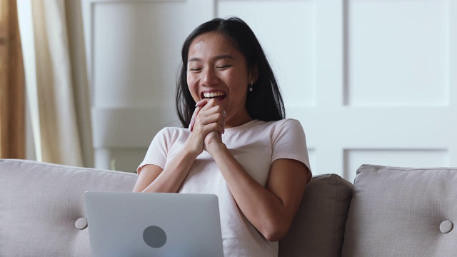 兴奋幸运的亚洲女人使用笔记本电脑坐在沙发上视频素材