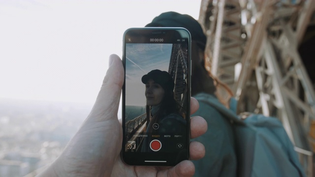 一名男子正在用智能手机拍摄埃菲尔铁塔上一名快乐微笑的女子的视频。浪漫概念慢动作。视频素材