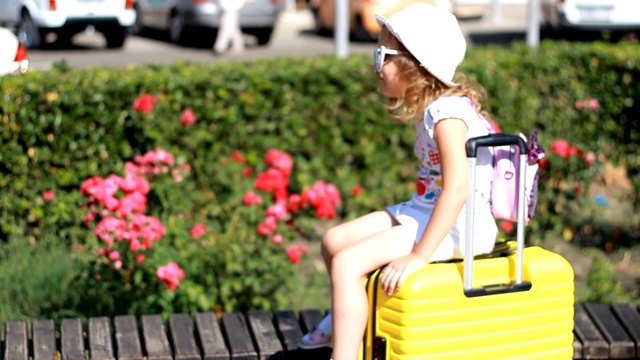 女游客坐在一个黄色的大行李箱上。等待旅行的孩子。视频下载